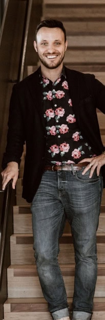 Smiling man with dark hair and beard, wearing a floral shirt and blazer.