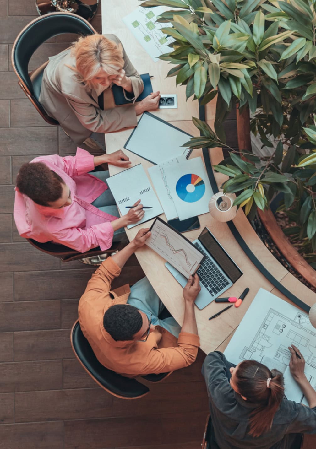 High-angle view of diverse team collaborating on data and design projects at a wooden table.