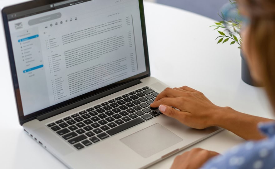 Email inbox on a laptop screen, person reading email on MacBook, digital communication, office workspace.