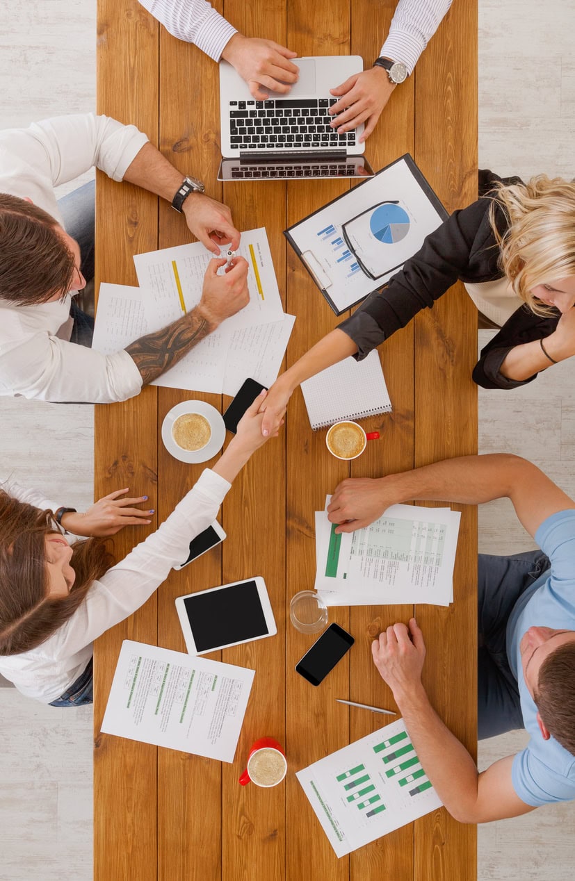 Brochure Style Meeting Over Business Documents and Digital Devices on Wooden Table.