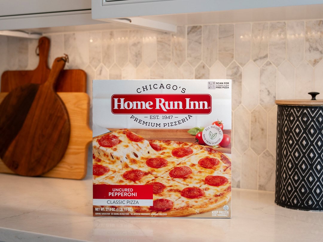 Pepperoni pizza box on kitchen countertop with chopping boards and decorative container.
