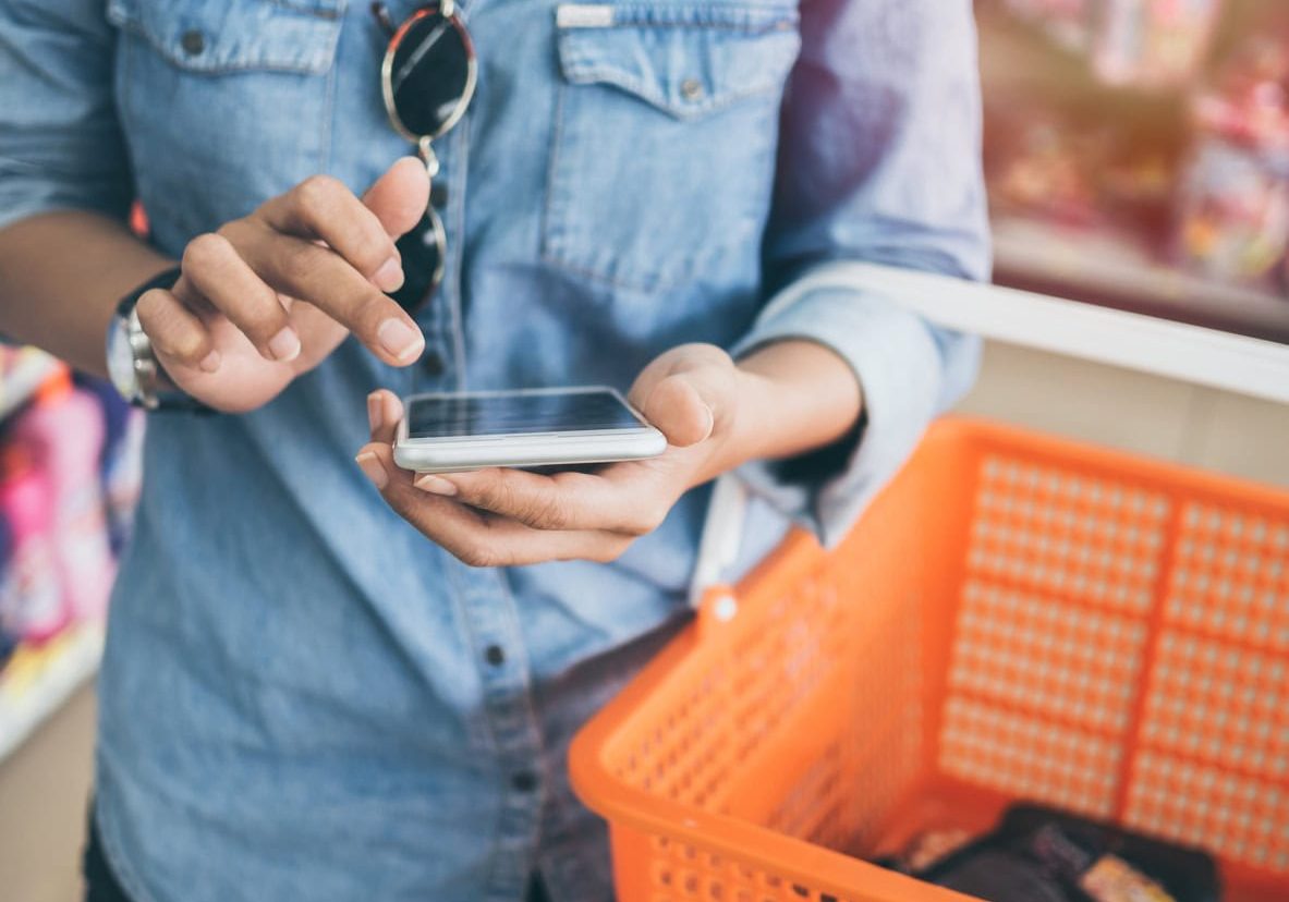 Mobile shopping in a grocery store, person using smartphone to browse products.