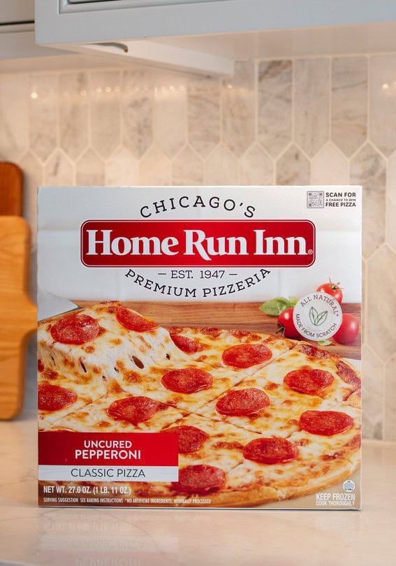 Pepperoni pizza box on kitchen countertop with chopping boards and decorative container.